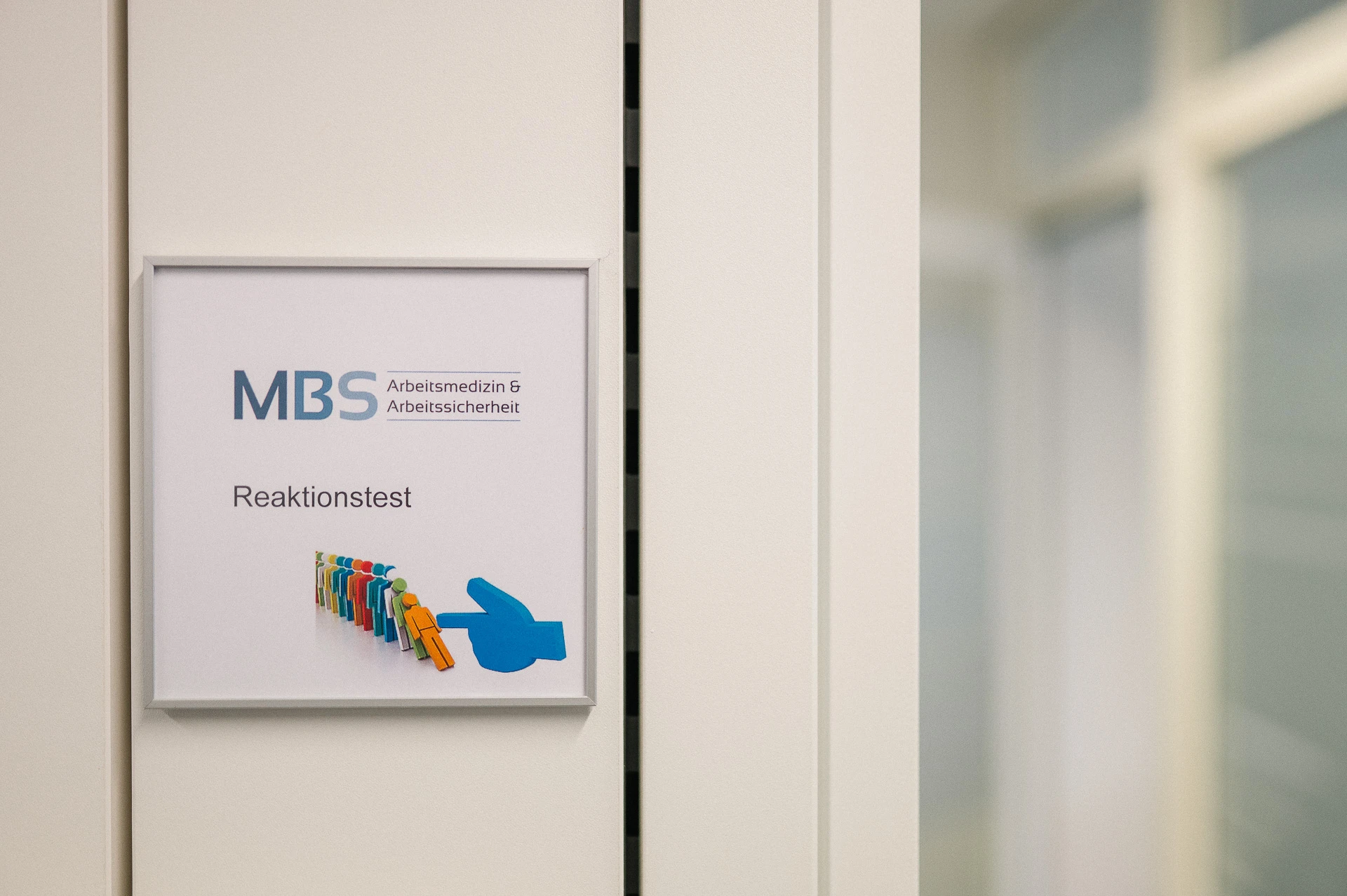Schild mit Aufschrift Reaktionstest und MBS-Logo an der Wand neben einem Untersuchungsraum
