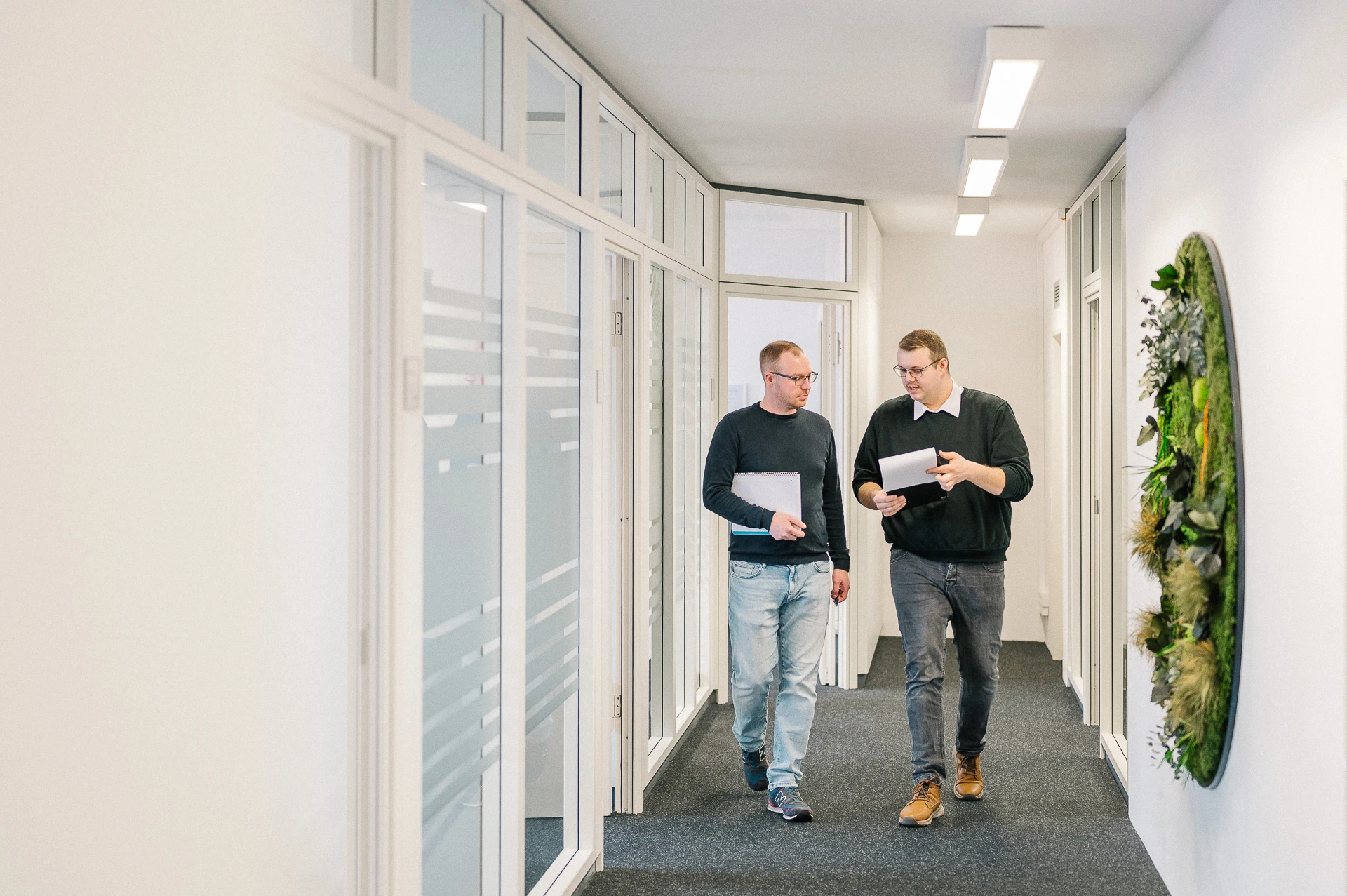 Zwei MBS-Mitarbeitende gehen durch den Flur der Freiburger Zentrale und besprechen Unterlagen